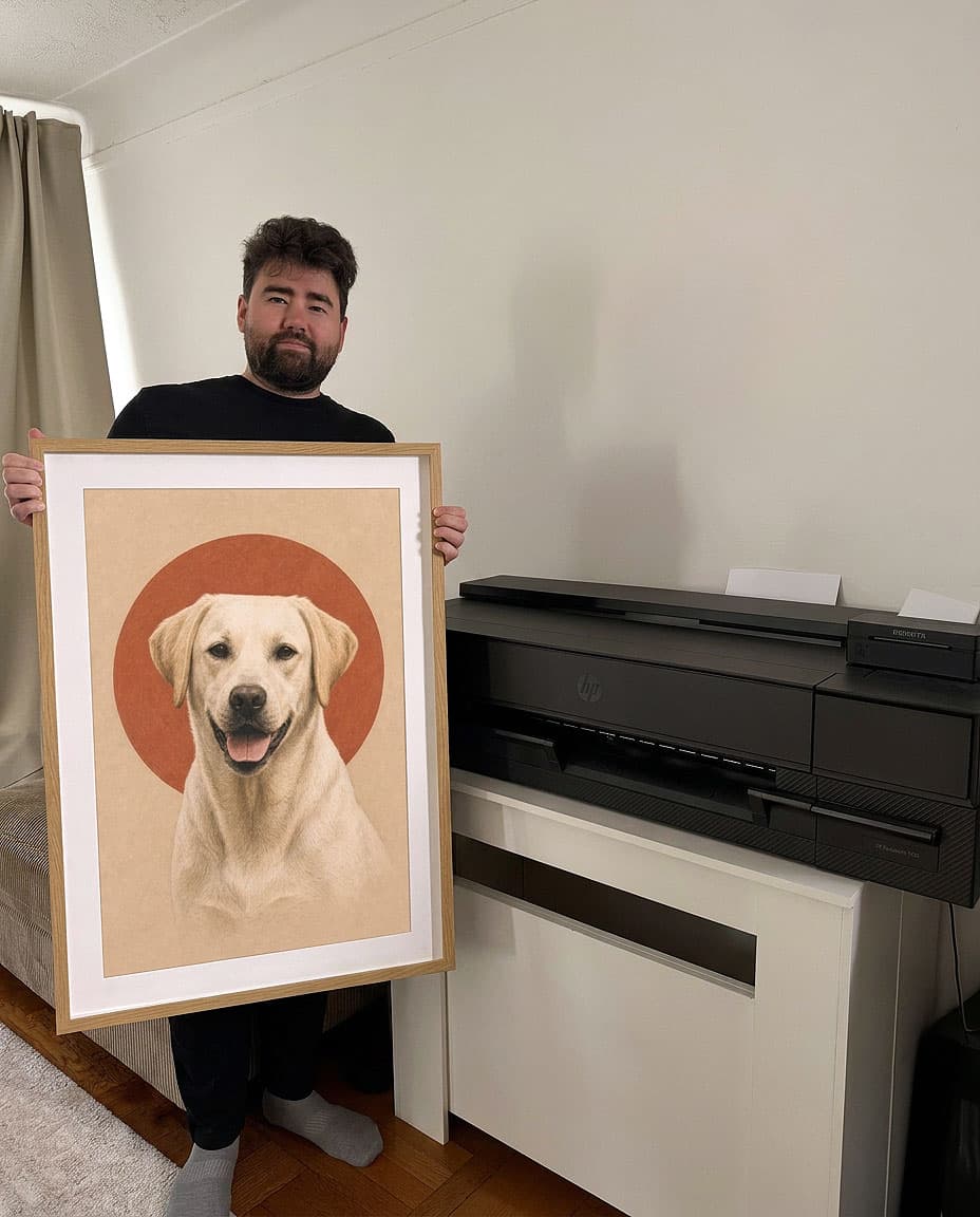Ramil holding a framed Labrador portrait beside the HP DesignJet he prints on, in the Bay Ridge studio